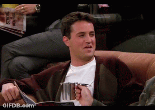 A Man Sits On A Couch Reading A Magazine And Holding A Cup GIF