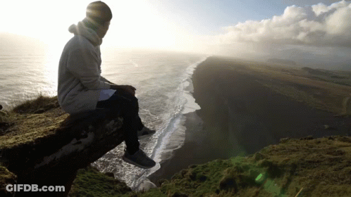 A Man Sits On A Ledge Overlooking The Ocean GIF