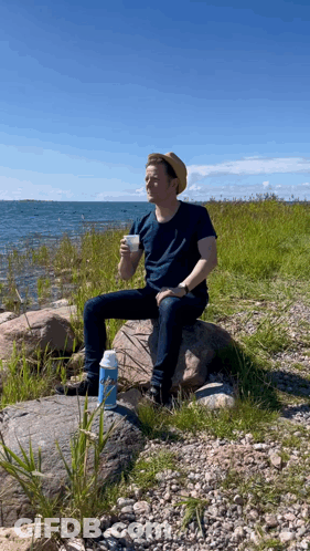 A Man Sits On A Rock Drinking From A Thermos GIF