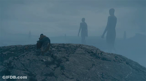 A Man Sits On A Rock In Front Of A Group Of Giant Silhouettes GIF