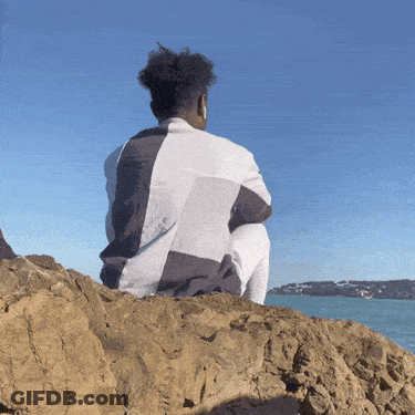 A Man Sits On A Rock Looking Out Over The Ocean GIF