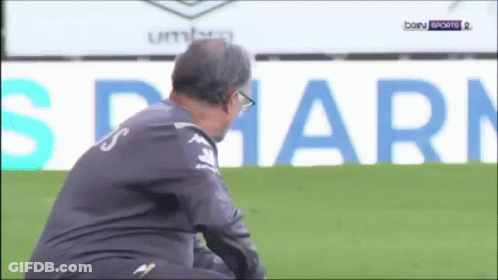 A Man Sits On A Soccer Field In Front Of An Ad For Bein Sports 2 GIF