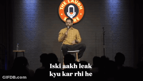 A Man Sits On A Stage In Front Of A Sign That Says " The Laugh Store " GIF