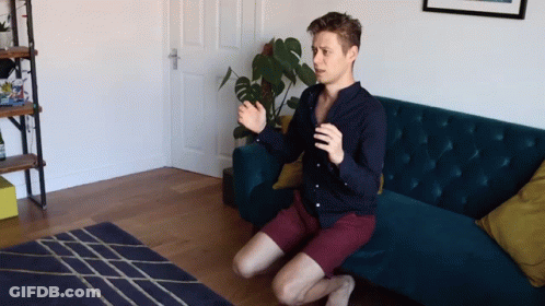 A Man Sits On His Knees In Front Of A Couch GIF