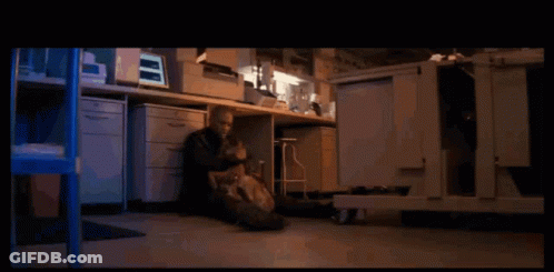 A Man Sits On The Floor In Front Of A Desk With A Computer Monitor On It GIF