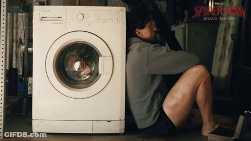 A Man Sits On The Floor Next To A Washing Machine That Says Spider-Man Brand Now On It GIF