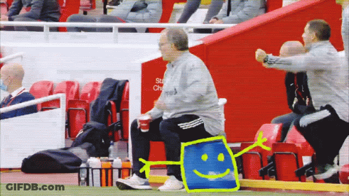 A Man Sits On The Sidelines Of A Soccer Game With A Smiley Face Drawn On A Blue Bag GIF