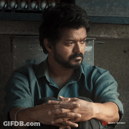 A Man Sits With His Hands Folded In Front Of A Sony Music Ad GIF