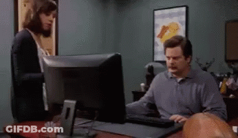 A Man Sitting At A Desk Using A Computer With A Woman Standing Behind Him GIF