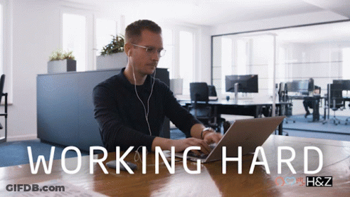 A Man Sitting At A Desk With A Laptop And The Words Working Hard On The Bottom GIF
