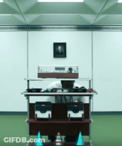 A Man Sitting At A Desk With A Picture Of A Man On The Wall Above Him GIF
