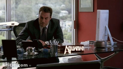 A Man Sitting At A Desk With A Sign That Says Aquafina GIF