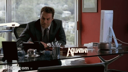 A Man Sitting At A Desk With A Sign That Says Aquafina GIF