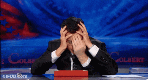 A Man Sitting At A Desk With His Hands On His Head In Front Of A Colbert Sign GIF