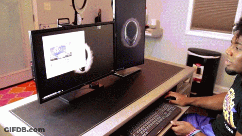 A Man Sitting At A Desk With Two Monitors And A Trash Can In The Background GIF