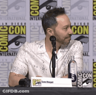 A Man Sitting At A Table At Comic Con GIF