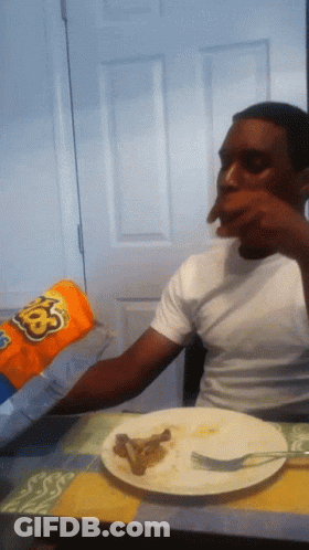 A Man Sitting At A Table Eating A Bag Of Cheetos GIF
