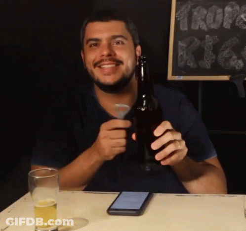 A Man Sitting At A Table Holding A Beer Bottle GIF