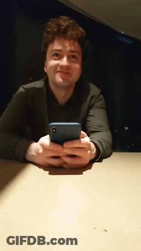A Man Sitting At A Table Holding A Cell Phone In His Hands GIF