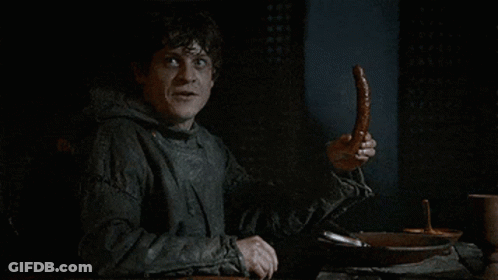 A Man Sitting At A Table Holding A Sausage In His Hand . GIF