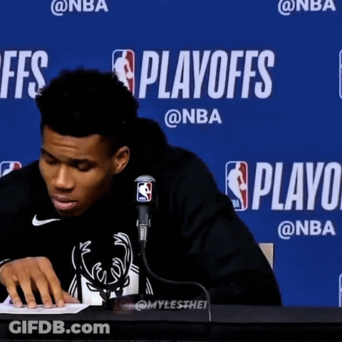 A Man Sitting At A Table In Front Of A Blue Wall That Says Playoffs On It GIF
