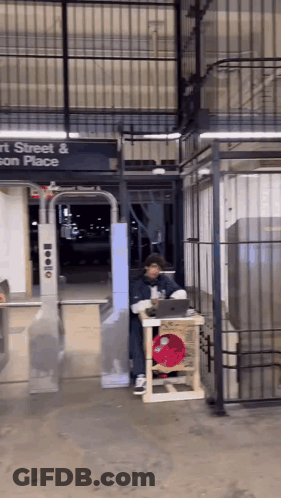 A Man Sitting At A Table In Front Of A Sign That Says Street And Son Place GIF