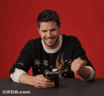 A Man Sitting At A Table Looking At A Cell Phone With The Words That 'S Funny On The Bottom GIF