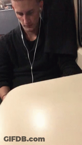 A Man Sitting At A Table Wearing Ear Buds GIF