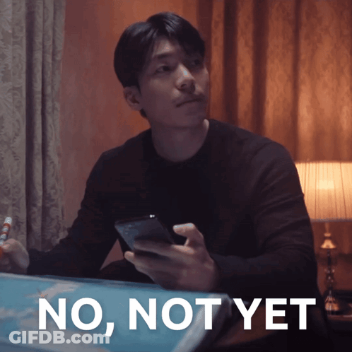 A Man Sitting At A Table With A Cell Phone In His Hand And The Words No Not Yet Behind Him GIF