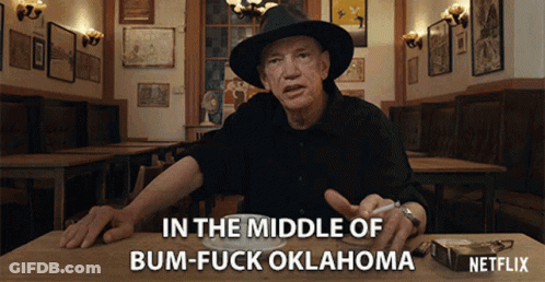 A Man Sitting At A Table With A Cigarette In His Hand Says In The Middle Of Bum-Fuck Oklahoma Netflix GIF