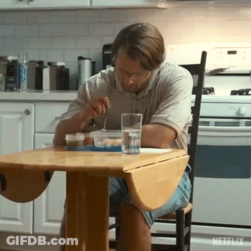 A Man Sitting At A Table With A Glass Of Water And A Bowl Of Food GIF