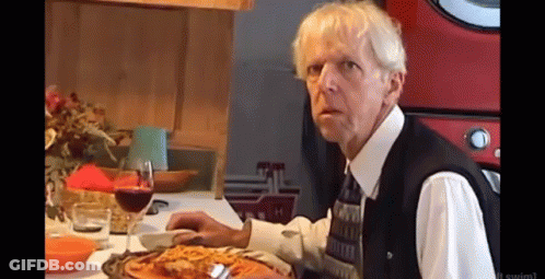 A Man Sitting At A Table With A Glass Of Wine And A Plate Of Pizza GIF