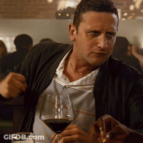 A Man Sitting At A Table With A Glass Of Wine In Front Of Him GIF