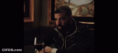 A Man Sitting At A Table With A Glass Of Wine In His Hand GIF