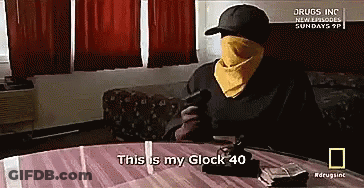 A Man Sitting At A Table With A Gun And Says This Is My Glock 40 GIF