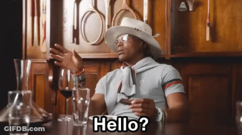 A Man Sitting At A Table With A Hat And Glasses Says Hello GIF