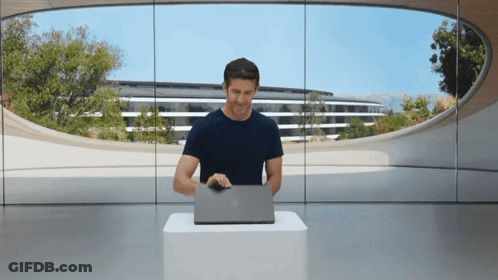 A Man Sitting At A Table With A Laptop In Front Of A Large Window GIF