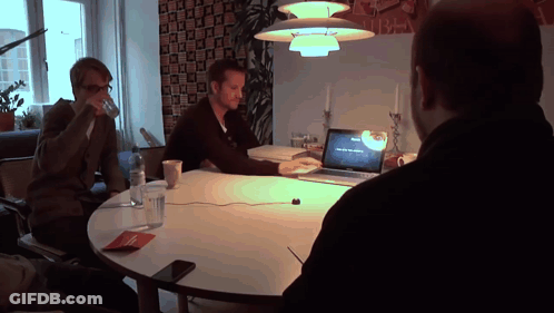 A Man Sitting At A Table With A Laptop That Says ' Macbook Pro ' On The Screen GIF