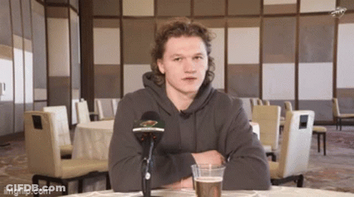 A Man Sitting At A Table With A Microphone And A Glass Of Beer . GIF