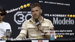 A Man Sitting At A Table With A Microphone In Front Of A Sign That Says Modelo GIF