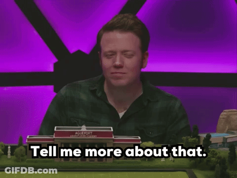 A Man Sitting At A Table With A Model Of A School Behind Him And The Words Tell Me More About That GIF
