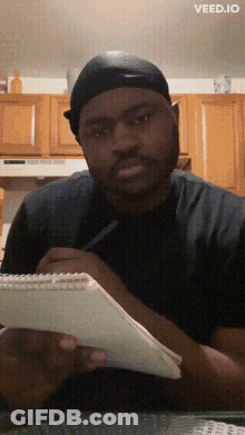 A Man Sitting At A Table With A Notebook And A Pen And The Words Veed.io On The Bottom Right GIF