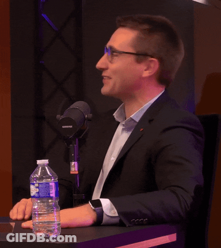 A Man Sitting At A Table With A Shure Microphone GIF