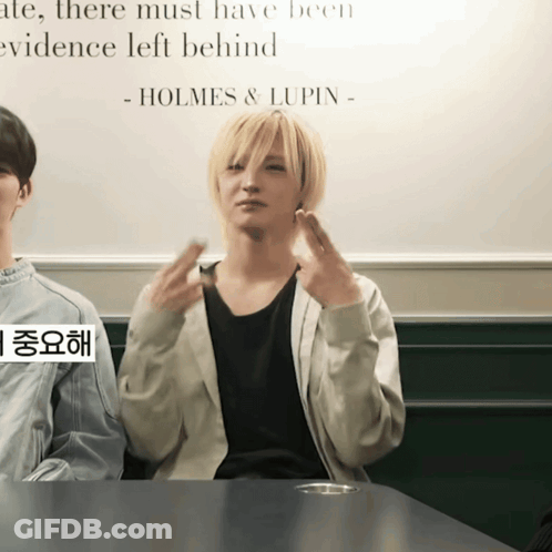 A Man Sitting At A Table With A Sign That Says Holmes & Lupin GIF