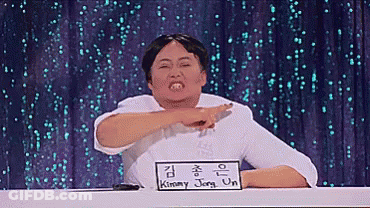 A Man Sitting At A Table With A Sign That Says Kimmy Jong-Un On It GIF