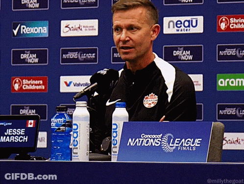 A Man Sitting At A Table With A Sign That Says Nations League Finals GIF