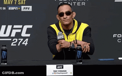 A Man Sitting At A Table With A Sign That Says Ufc GIF