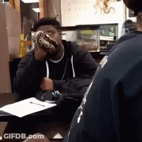 A Man Sitting At A Table With A Snake On His Face GIF