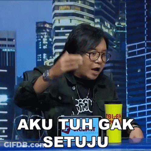 A Man Sitting At A Table With A Yellow Cup That Says Aku Tuh Gak Setuju On It GIF