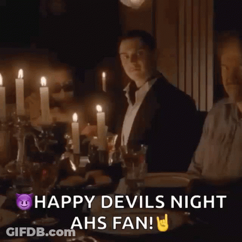 A Man Sitting At A Table With Candles And The Words Happy Devils Night Ahs Fan On The Bottom GIF
